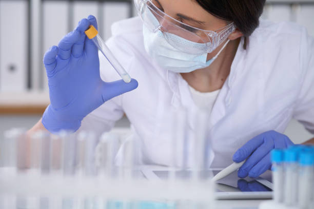 close-up of professional female scientist in protective eyeglasses making experiment with reagents in laboratory. medicine and research concept - close up medical test exam people imagens e fotografias de stock