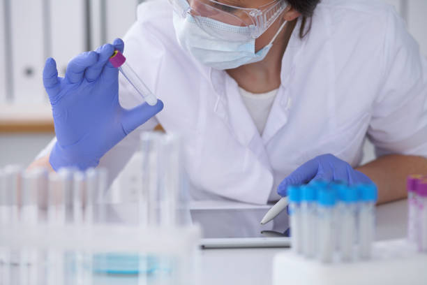 close-up of professional female scientist in protective eyeglasses making experiment with reagents in laboratory. medicine and research concept - close up medical test exam people imagens e fotografias de stock