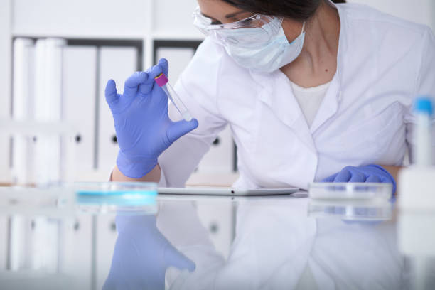 close-up of professional female scientist in protective eyeglasses making experiment with reagents in laboratory. medicine and research concept - close up medical test exam people imagens e fotografias de stock