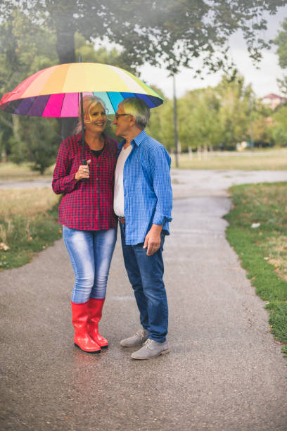 senior couple with a rainbow umbrella - umbrella senior adult couple autumn imagens e fotografias de stock