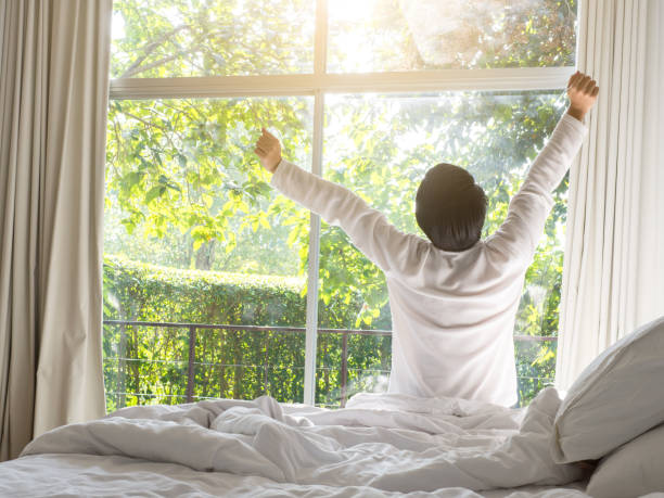 leniwy człowiek szczęśliwy budząc się w łóżku wznoszące się ręce do okna rano ze świeżym uczuciem relaksu - good morning zdjęcia i obrazy z banku zdjęć