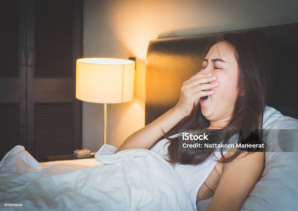 Young beautiful asian woman yawn and feeling sleepy on white bed in bed room. Yawning Stock Photo