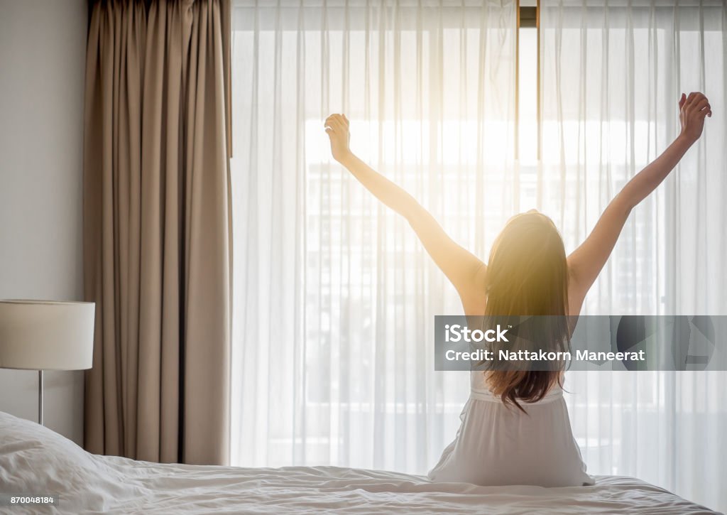 Femme asiatique réveille le matin, assis sur le lit blanc et qui s’étend, se sentir heureux et frais - Photo de Se réveiller libre de droits
