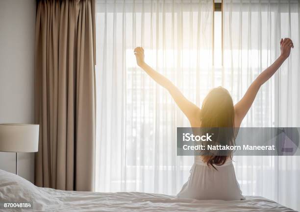アジアの女性は朝白いベッドの上に座ってストレッチ幸せと新鮮な気分を覚ます - 起床するのストックフォトや画像を多数ご用意 - 起床する, 眠る, 女性