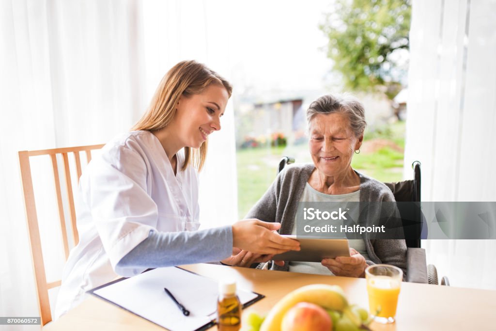 Health visitor and a senior woman with tablet. Health visitor and a senior woman with tablet during home visit. A nurse talking to an elderly woman. Home Caregiver Stock Photo