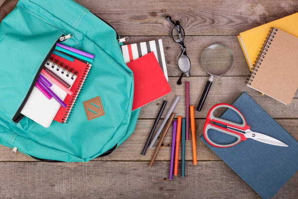 istock Backpack and school supplies: books, magnifying glass, notepad, felt-tip pens, eyeglasses, scissors on brown wooden table 870061040