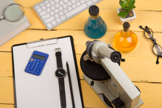 istock Education and science concept - microscope, book, magnifying glass, calculator, watch, blank clipboard, computer keyboard, eyeglasses and chemical liquids 870061148