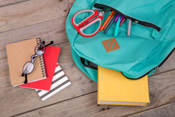 istock Backpack and school supplies: books, pencils, notepad, felt-tip pens, eyeglasses, scissors on brown wooden table 870064132