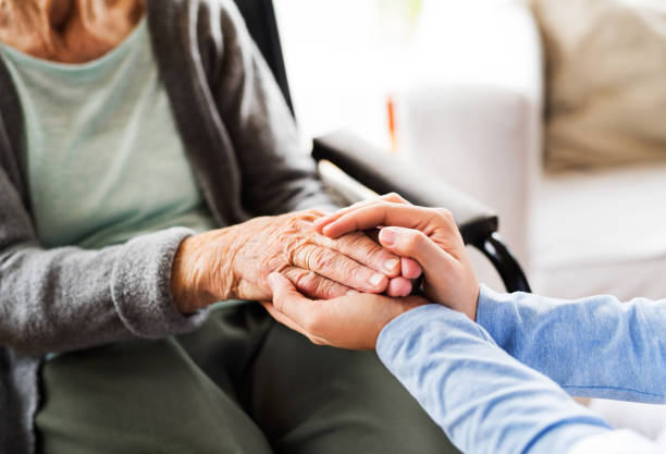 Unrecognizable health visitor and a senior woman during home visit. Unrecognizable health visitor and a senior woman during home visit. Nurse holding both hands of an eldelry woman. Close up. medical supplies wheelchair medical equipment nursing home stock pictures, royalty-free photos & images