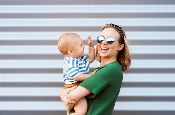 giovane donna con un bambino in piedi contro il muro. - sunglasses women smiling portrait foto e immagini stock