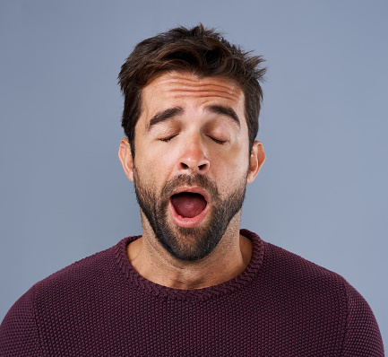 Studio shot of a handsome young man yawning against a gray background