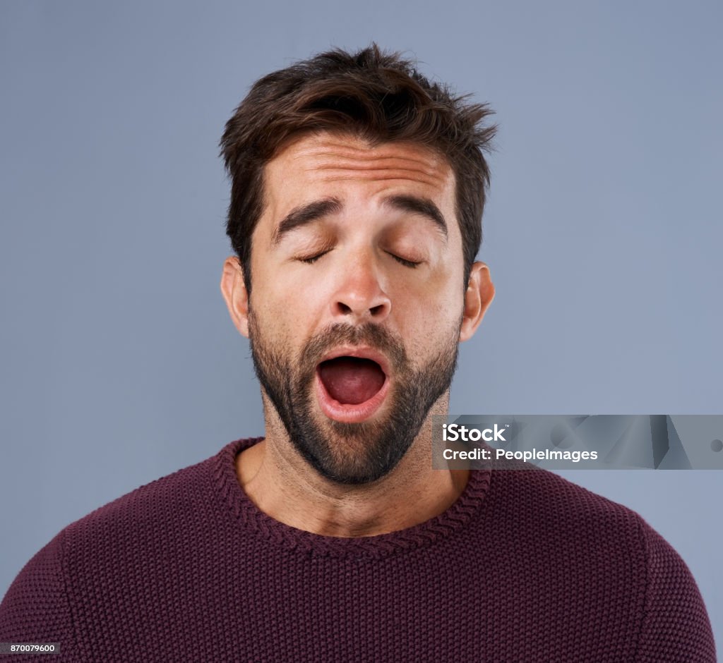 Is this day over yet? Studio shot of a handsome young man yawning against a gray background Yawning Stock Photo