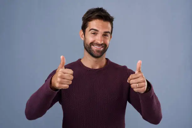 Studio shot of a handsome young man giving a thumbs up gesture against a gray background