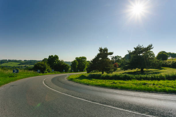istock Empty asphalt curvy road passing through green fields and forests. Countryside landscape on a sunny spring day in France. Sunbeams in the sky. Transport, industrial agriculture, road network concept 870083142