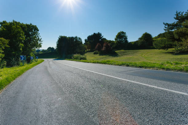 istock Empty asphalt country road passing through green fields and forest. Countryside landscape on sunny day with sunbeams in the blue sky in France. Transport, industrial agriculture, road network concept. 870083614
