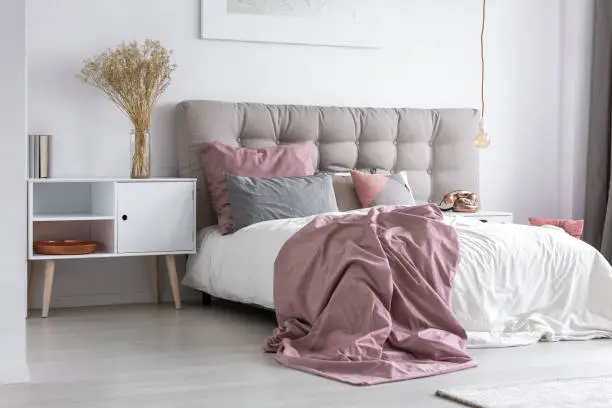 Gray tufted headboard and pink bedcover in simple bedroom with minimalist interior design and copper accessories