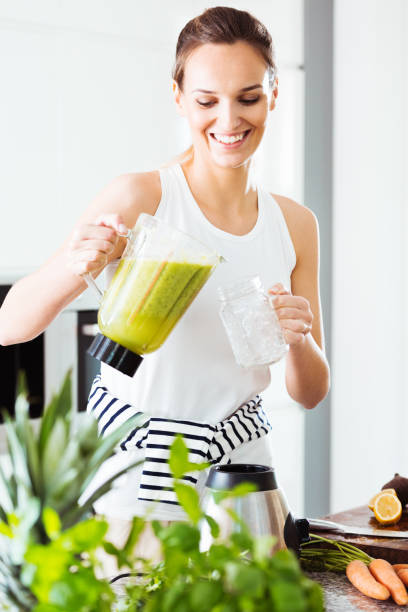 fit kobieta wylewa zielony koktajl - vegan food cheerful vertical indoors zdjęcia i obrazy z banku zdjęć