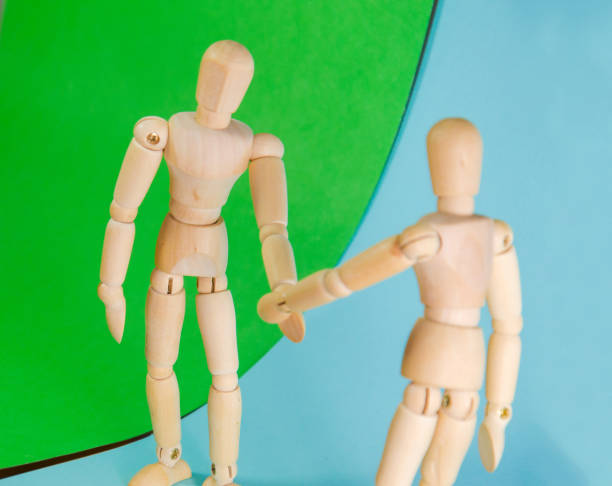istock Two wooden figure dolls doing a handshake over a blue green background 870129604