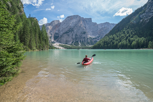 View of a young man canoeing on beautiful mountain lake in the Dolomites, Italy. Lago di Braies or Lake Braies.