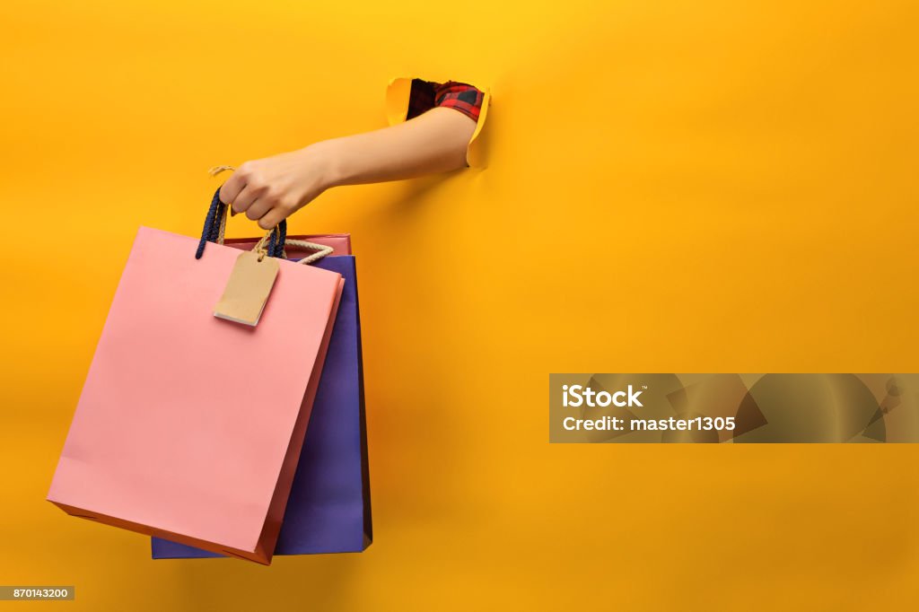 Female hand holding bright shopping bags Female hand holding bright shopping bags on yellow Retail Stock Photo