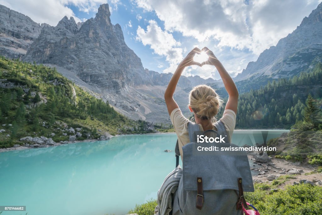 Love nature mountain heart shape concept, female loving Dolomites Young woman making heart shape finger frame on Alpine lake in Alto Adige region, Italy. Vacations Stock Photo