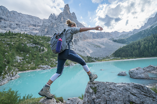 Young woman hiker jumping from rock to rock on mountain lake, Alto Adige, Dolomites, Italy
