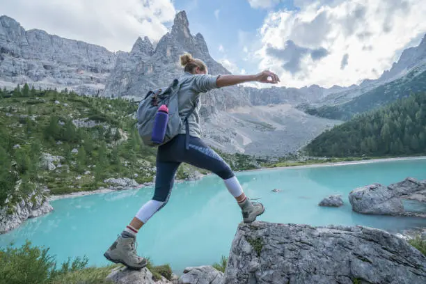 Photo of Young woman jumps rock to rock near mountain lake, Dolomites, Italy