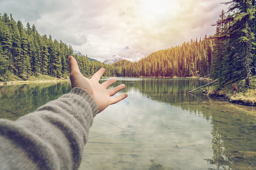 Pov of human hand stretching towards the sun at sunset. People travel hope environment concept