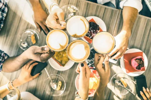 Photo of Friends group drinking cappuccino at coffee bar restaurant - People hands toasting at fashion cafeteria with upper view point - Winter drinks concept with men and women at cafe - Warm vintage filter