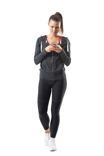 Young athletic female runner in sportswear using cell phone. Full body length portrait isolated on white background.