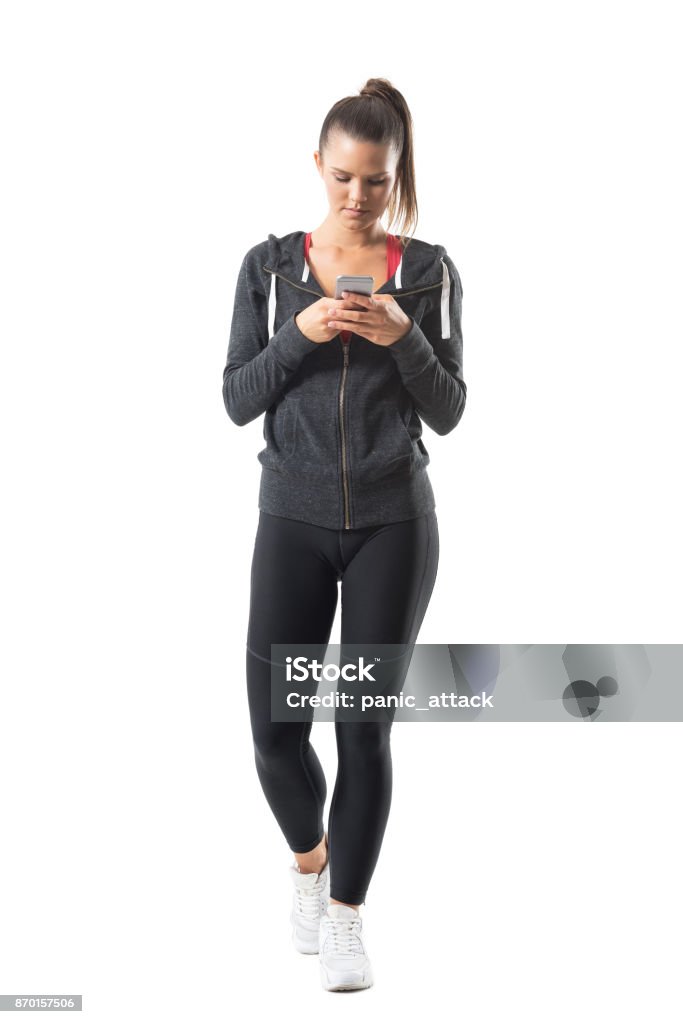 Young athletic female runner in sportswear using cell phone. Young athletic female runner in sportswear using cell phone. Full body length portrait isolated on white background. Cut Out Stock Photo