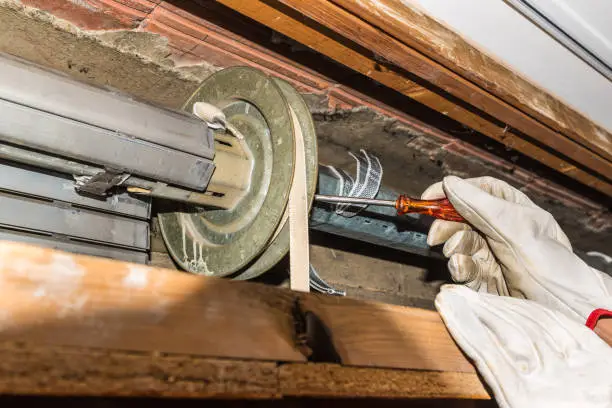 Close-up of hands with gloves of a rolling shutter repair and orange starter screwdriver