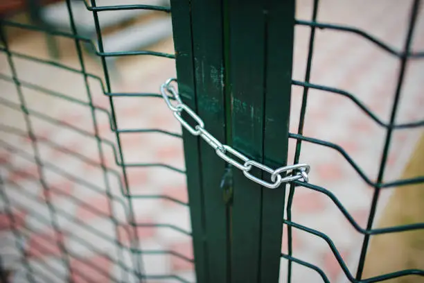 Close up metallic net-shaped green fence that closed and wrapped by chain.
