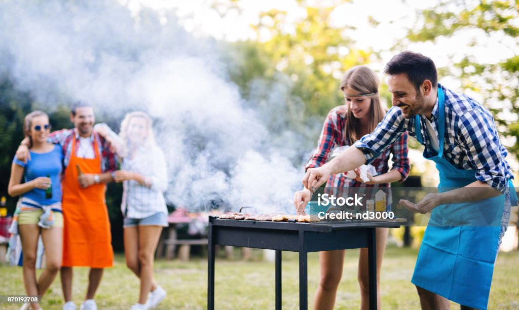 Young people grilling outdoors Young happy people enjoying barbecuing in forest Barbecue - Meal Stock Photo