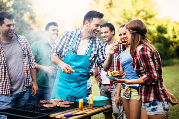 szczęśliwi przyjaciele cieszący się imprezą przy grillu - barbecue spotkanie towarzyskie zdjęcia i obrazy z banku zdjęć