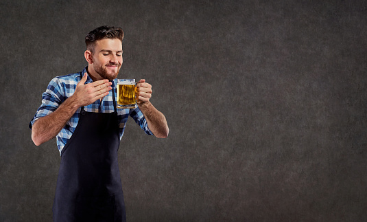 The brewer in his apron sniffs the smell of freshly brewed beer on the copy spase background.