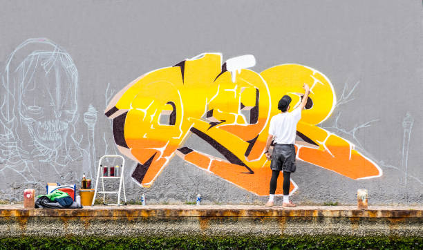 street artist che dipinge graffiti colorati sulla parete dello spazio pubblico - concetto di arte moderna del ragazzo urbano che esegue e prepara murales dal vivo dipingere con spray giallo aerosol colore - filtro pomeridiano nuvoloso - spray paint spray paint graffiti foto e immagini stock