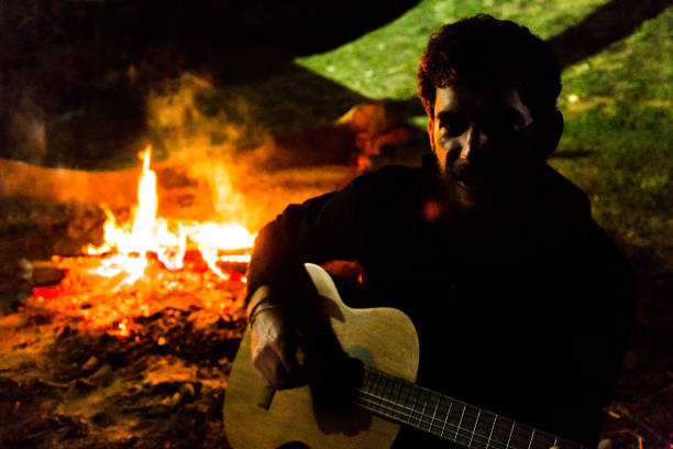 istock Young man playing acoustic guitar by the fire 870206726