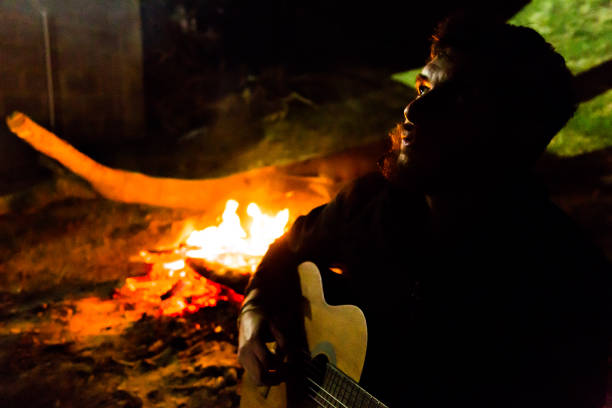istock Young man playing acoustic guitar by the fire 870206970