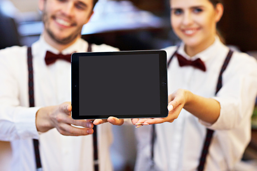 Waiters standing in restaurant holding digital tablet
