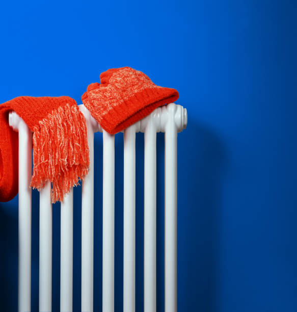 оранжевый трикотаж шапку и шарф, лежащий на белом радиаторе отопления на фоне синей стены - knitting vertical striped textile стоковые фото и изображения