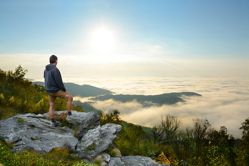 Man standing  a top of mountain relaxing. and looking at beautiful foggy mountain landscape at sunrise .  Near Asheville, Blue Ridge Mountains, North Carolina, USA.