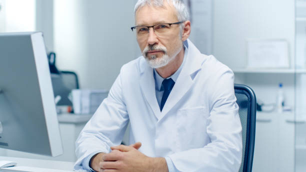 istock Experienced Gray Haired Senior Medical Practitioner Looking Into Camera. Portrait Shot in Modern and Light Office. 870233572