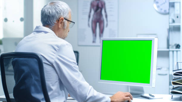 自分のパソコンに緑色の画面で取り組んでシニア男性研究室研究員。モックの大アップ。 - language therapy ストックフォトと画像
