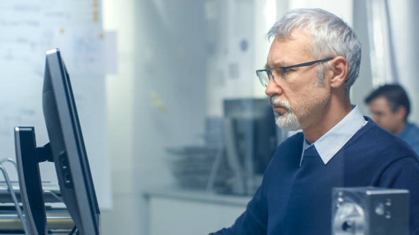 istock Close-up Shot of a Chief Engineer Working at His Desk, Some Technical Components Lying on His Desk. His Assistant Works at His Desk in the Background. 870233626