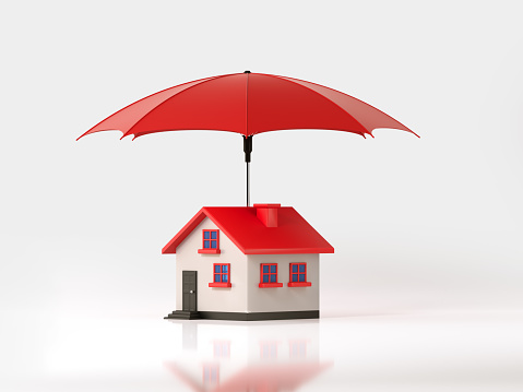 Red umbrella is protecting a toy house on white background. Horizontal composition with selective focus and copy space. Insurance and real estate concept.