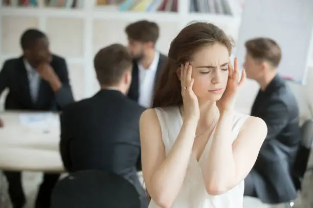Stressed young female corporate employee having migraine at unproductive briefing. Business woman got headache from stressful meeting, coworkers not collaborating. Female executive sick from stress.