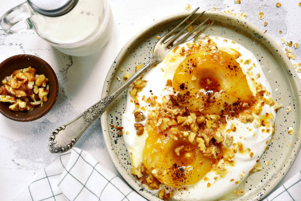 Caramelized pear with nuts and yogurt Caramelized pear with nuts and yogurt for a breakfast on a rustic craft plate over white slate,stone or concrete background.Top view. pear dessert stock pictures, royalty-free photos & images