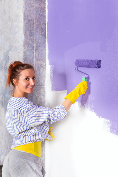 istock woman paints white wall purple paint roller 870295792