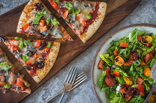 Sliced pizza on a board with balsamic salad